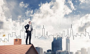 Kararlı genç işadamı evin çatısında dikiliyor ve başka tarafa bakıyor. Karışık ortam