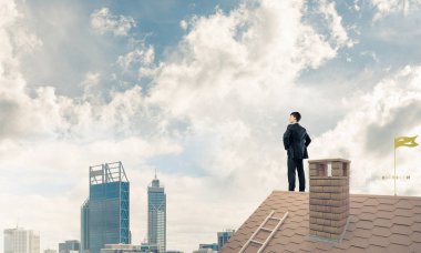 Kararlı genç işadamı evin çatısında dikiliyor ve başka tarafa bakıyor. Karışık ortam