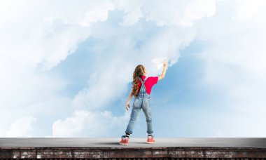 Binanın tepesinde kağıt uçakla oynayan sevimli, mutlu bir kız.