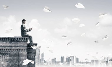 Elinde cep telefonu ile üst yapı üzerinde oturan genç işadamı