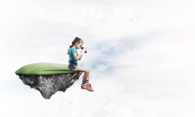 Gökyüzünde yüzen bir adada oturan tatlı, gülümseyen bir kız.