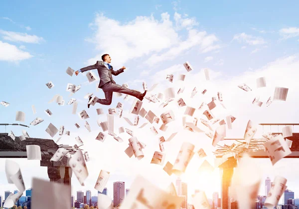 Businessman jumping over gap with flying paper documents in concrete bridge as symbol of overcoming challenges. Cloudly with sunlight skyscape on background. 3D rendering.