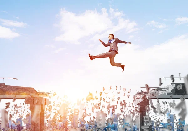 Businessman jumping over gap with flying letters in concrete bridge as symbol of overcoming challenges. Cityscape with sunlight on background. 3D rendering.