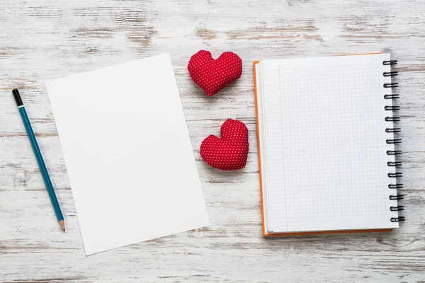 Hearts and blank notepad with pencil on wooden table