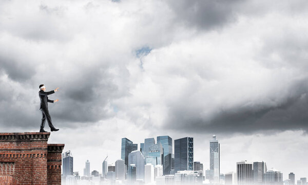 Businessman with blindfolder on eyes walking on building top