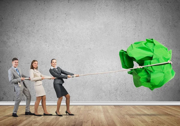 Office employees pulling together big crumpled paper ball