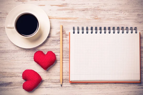 Coffee cup notepad pencil and two red hearts on wooden surface