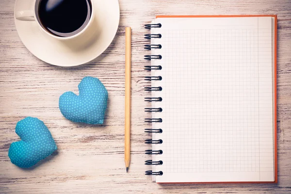 Coffee cup notepad pencil and two hearts on wooden surface