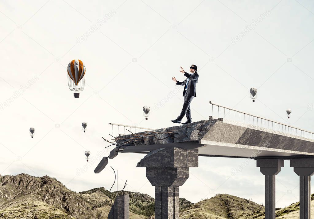 Businessman walking blindfolded on concrete bridge with huge gap as symbol of hidden threats and risks. Flying balloons and nature view on background. 3D rendering.