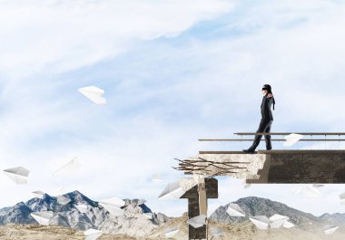 Gizli tehditlerin ve risklerin sembolü olarak beton köprüde gözü kapalı yürüyen bir iş adamı. Arka planda gökyüzü ve doğa manzarası. 3B görüntüleme.