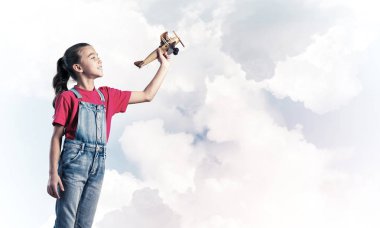 Elinde retro uçak modeliyle tulumlu şirin bir kız çocuğu.