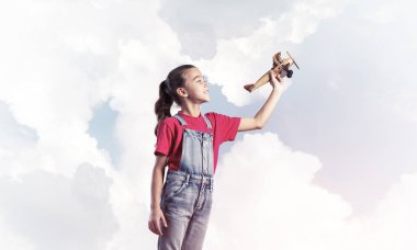 Elinde retro uçak modeliyle tulumlu şirin bir kız çocuğu.