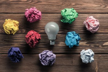 Birden çok renkli crampled kağıt topu ve ampul aralarında, yeni fikirlerden arama aracı olarak ahşap masanın üzerine yerleştirilen.