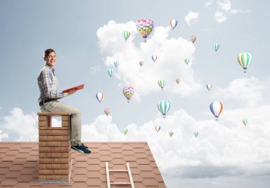 Elinde kırmızı kitap ile evin baca rahat oturan genç adam