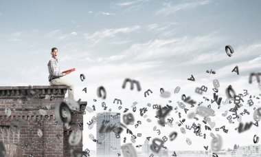 Elinde kırmızı kitap ile üst yapı üzerinde rahat oturan genç adam