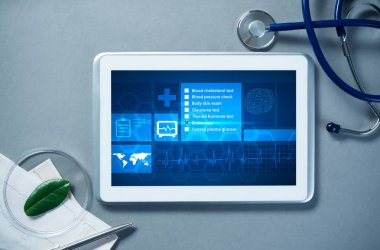 Gri yüzeyde beyaz tablet ve doktor araçları