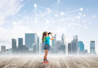 Şirin kız ahşap bir zeminde duruyor ve dürbünle izliyor.