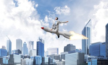 Arka plan üzerinde modern cityscape gökdelenler ve mavi gökyüzü ile roket üzerinde uçan takım elbiseli Genç ve mutlu işadamı kavramsal görüntü.