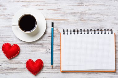 Kahve fincanı not defteri kalem ve ahşap yüzeyde iki kırmızı kalp