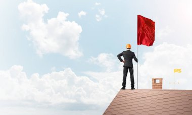 Çatıda duran ve elinde kırmızı bayrak tutan bir iş adamı. Karışık ortam