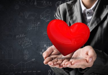 Kırpılmış görüntü arka plan üzerinde koyu duvar skeçler ile elleri büyük kırmızı kalp sunan takım elbiseli işadamı. 3D render.