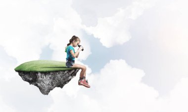 Gökyüzünde yüzen bir adada oturan tatlı, gülümseyen bir kız.