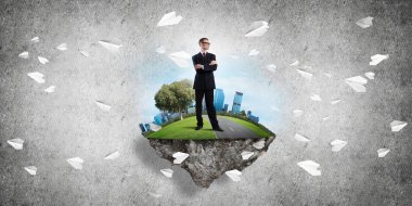 Yeşil yüzen adada beton zemine karşı duran kendine güvenen zarif iş adamı.