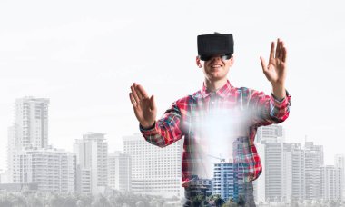 Sanal gerçeklik kulaklığı olan genç bir adam ya da şehrin arka planında 3 boyutlu gözlüklü.