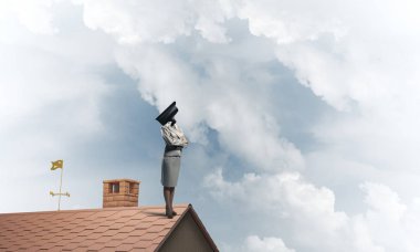 Evin çatısında baş durmak yerine kamerayla zum yapan yüzsüz iş kadını.