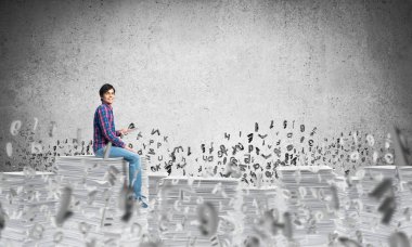 Gri duvar harflerle arka plan üzerinde uçan arasında casual giyim oturan genç adam. Karışık teknik.