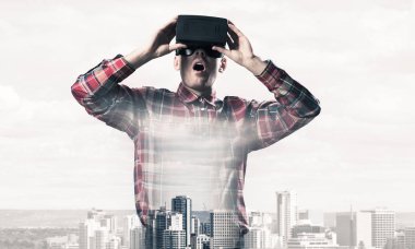 Sanal gerçeklik kulaklığı olan genç bir adam ya da şehrin arka planında 3 boyutlu gözlüklü.