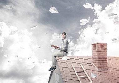 Elinde kırmızı kitap ile ev üzerinde oturan genç adam