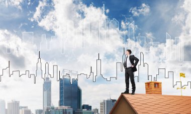 Kararlı genç işadamı evin çatısında dikiliyor ve başka tarafa bakıyor. Karışık ortam