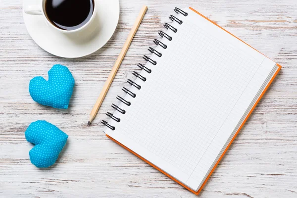 Coffee cup notepad pencil and two hearts on wooden surface