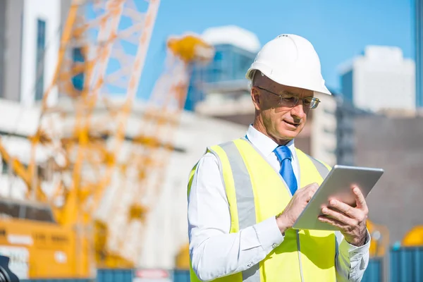 Senior engineer man in suit and helmet working on tablet pc