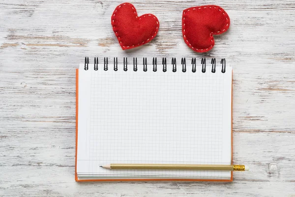 Hearts and blank notepad with pencil on wooden table