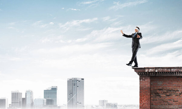 Businessman with blindfolder on eyes walking on building top