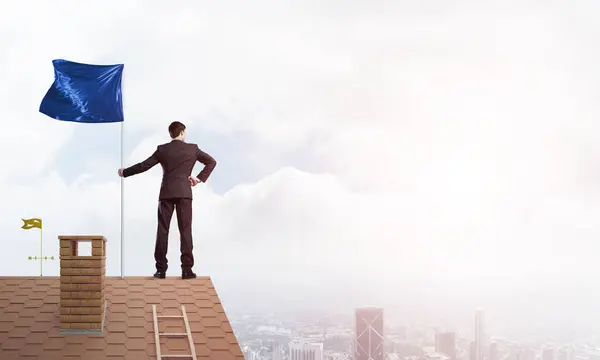 Businessman Standing House Roof Holding Blue Flag Mixed Media — Stock Photo, Image
