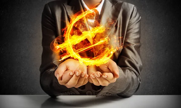彼の手で燃えるようなユーロ記号を呈する背景に暗い壁のスーツのビジネスマンのクローズ アップ — ストック写真