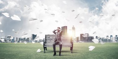 Hüsrana uğramış işadamı bankta oturuyor ve elleriyle kulaklarını kapatıyor.