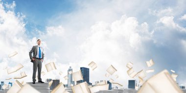 Kendine güvenen işadamı belgeleri kitap Clear sky ile arka plan üzerinde uçan arasında yığını üzerinde takım elbise ayakta. Karışık teknik.