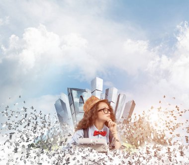 Genç kadın yazar şapka ve gözlük harfler yüzen Şehir Adası ve bulutlu gökyüzü arka plan üzerinde uçan arasında masadaki otururken yazarak makinasıyla.