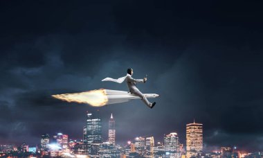 Arka plan üzerinde gece cityscape ve mavi gökyüzü ile roket üzerinde uçan takım elbiseli genç işadamı kavramsal görüntü.
