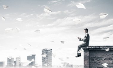 Elinde cep telefonu ile üst yapı üzerinde oturan genç işadamı