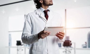 Beyaz steril önlük ayakta beyaz hastane ofis güneş ışığı ile arka plan üzerinde binası içinde kendine güvenen doktor görüntü kırpılmış.