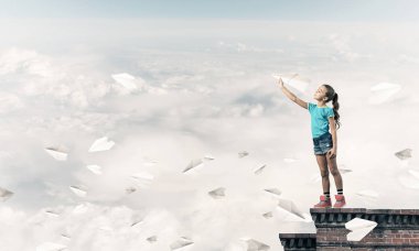 Binanın tepesinde kağıt uçakla oynayan sevimli, mutlu bir kız.
