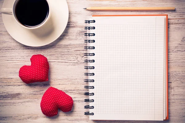 Coffee cup notepad pencil and two red hearts on wooden surface