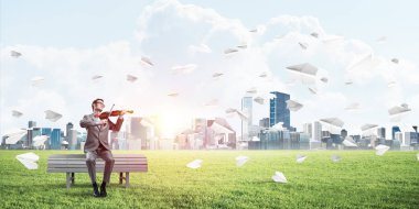 Takım elbiseli ve gözlüklü genç adam bankta oturup keman çalıyor.