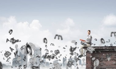 Elinde kırmızı kitap ile üst yapı üzerinde rahat oturan genç adam