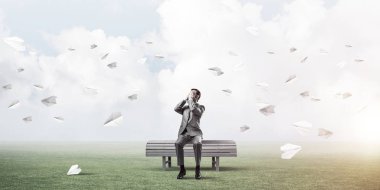 Şok olmuş genç işadamı ahşap bankta oturuyor ve gözleri palmiyelerle örtüyor.